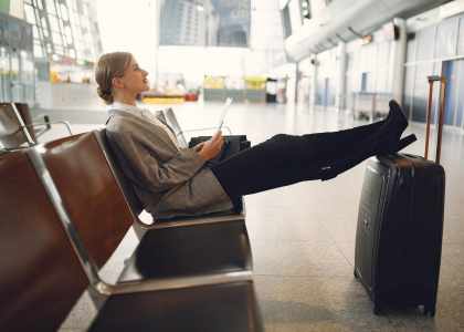 Femme détendu assise dans le hall de l'aéroport tendant ses jambes sur sa valise 