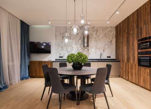 Salle à manger moderne avec suspension en verre, cuisine en bois et mur en marbre blanc.